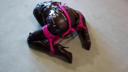 Adreena Booted Hooded And Straitjacketed  2 - In the second part of this video clip, adreena is still dressed from head to toes in fetish clothing. A severe pvc hood with a pink ballgag tops an outfit consisting of a heavy rubber straitjacket, rubber capri pants and thigh high corset boots.

a steel spreader bar is attached to adreena's ankles and pink ropes are added to the bondage to make it progressively harder for adreena to move around the floor.  Adreena does not enjoy being treated this way!