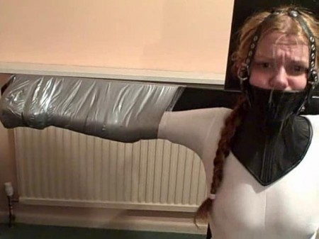 Fi In Supertight Bondage - Fi is wearing a skin-tight white catsuit paired with long leather gloves and knee-length ballet boots.  Mitts and cuffs are used to link her feet and hands to the wooden slave chair on which she sits.
plastic wrap is wrapped around each arm in turn, immediately followed by very tight wrappings of duct tape.  Fi struggles to escape but she appears as if glued to the cross of the slave chair.
the wrapping is completed in part 2.