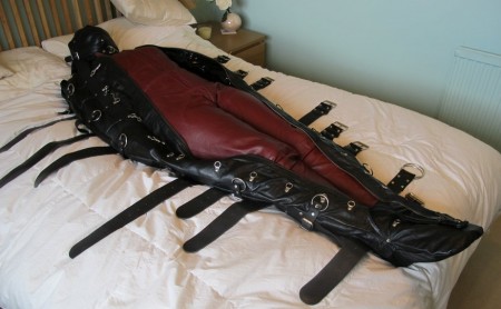 Tightened Into The Leather Bondage Bag - Karina is wearing her made-to-measure leather catsuit and the video opens with her inspecting the pvc-lined leather bondage bag that is lying on the bed.

after inspecting all the straps, buckles and other metalwork karina opens up the full-length zip, pulls on the leather sensory deprivation hood and climbs into the bodybag, making sure that her arms slide into the inner sleeves that will prevent any later movement.

we pull the zip up her body but it is a very tight fit and needs all the extra straps to be loosened before the zip can be fully closed.  Now the straps are retightened and karina can barely move.  However, those of you who have bought our clips before know that we are rarely satisfied where tightness is concerned and it is no time at all before, one-by-one, a set of thick leather straps are pushed, pulled and tightened at intervals up her body.

the leather hood is also relaced and fully tightened and all the straps buckled in place.  After taking some photographs the straps have warmed up and stretched a little.  As if we needed an excuse to tighten them further!

karina is encouraged to move within the body bag but her strenuous efforts are to no avail.  She will be going nowhere until we choose to release her!